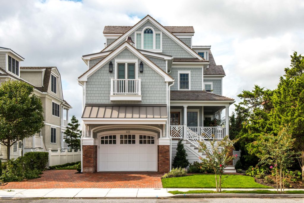 Beach house in Avalon, NJ, with gray shingles, white trim, and a covered porch. Features a two-car garage with brick accents and a well-maintained lawn.