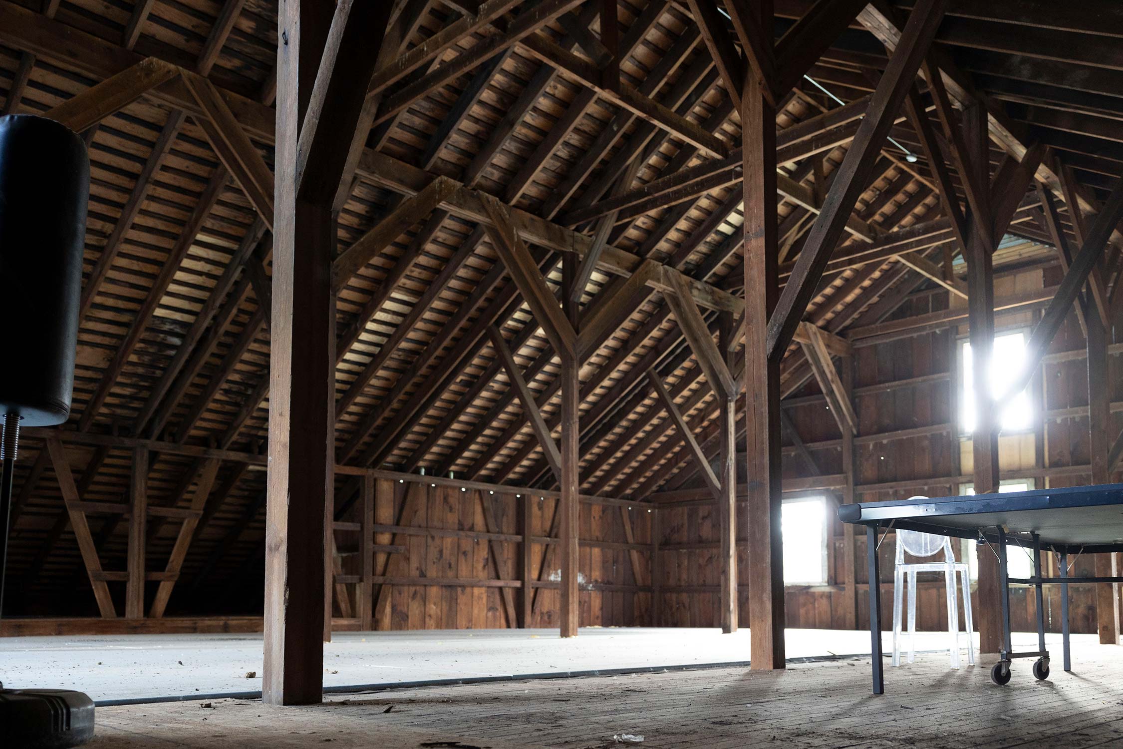 Interior of a wooden barn with exposed beams lit by natural light from windows.