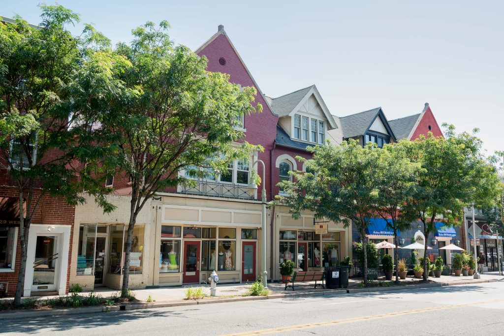 Street view of colorful storefronts in Adrmore, PA, including the Junior League of Philadelphia, with trees, benches, and outdoor seating.