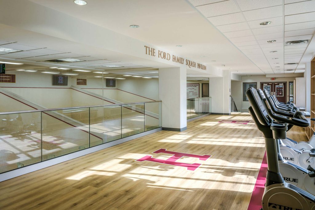 The Ford Family Squash Pavilion at The Haverford School with squash courts, glass walls, and exercise bikes. Features a hardwood floor with an 