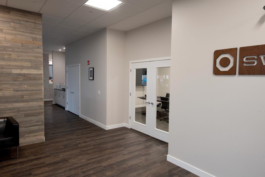 Modern office hallway at the Swisco headquarters with wooden floor, glass conference room, and a sign on the wall.