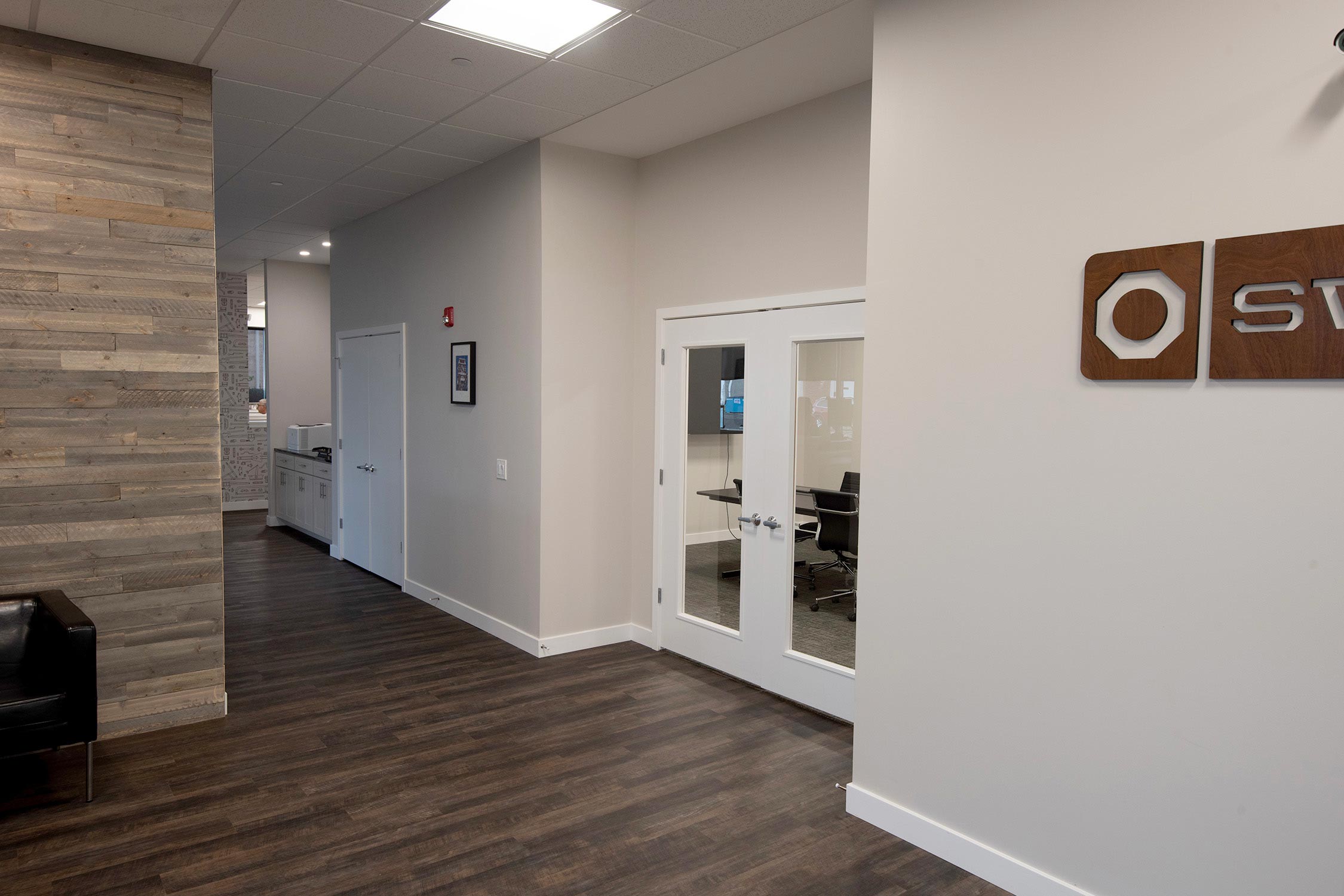 Modern office hallway at the Swisco headquarters with wooden floor, glass conference room, and a sign on the wall.