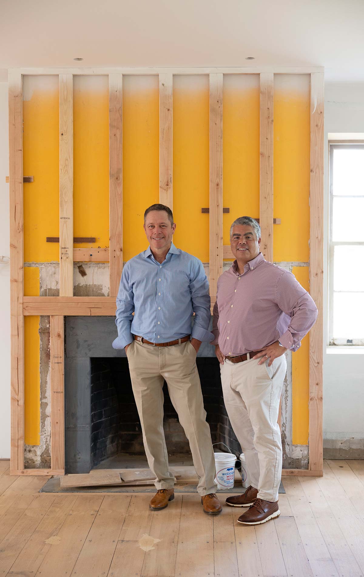 Andy Kerns and Greg Ranieri, Ranieri & Kerns founders, standing in front of a fireplace under construction in a room with wooden floors and white walls.
