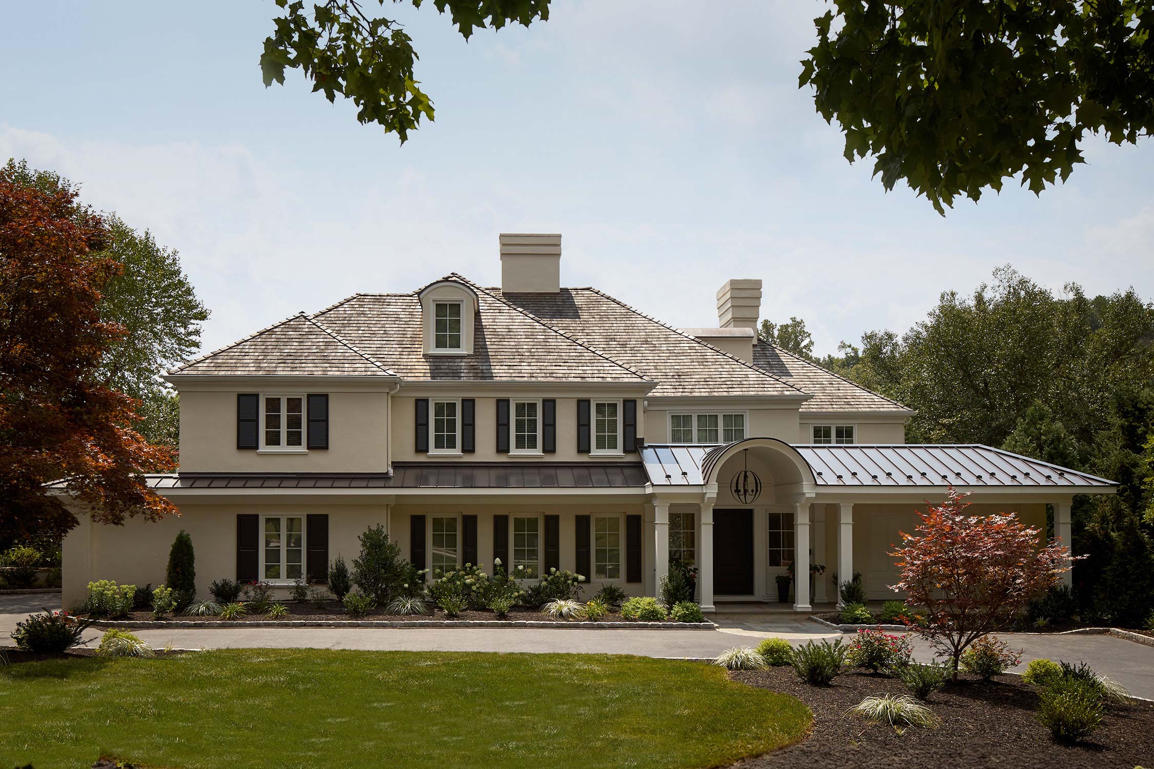 A large two-story house with a shingle roof, black shutters, covered porch, and landscaped front yard.