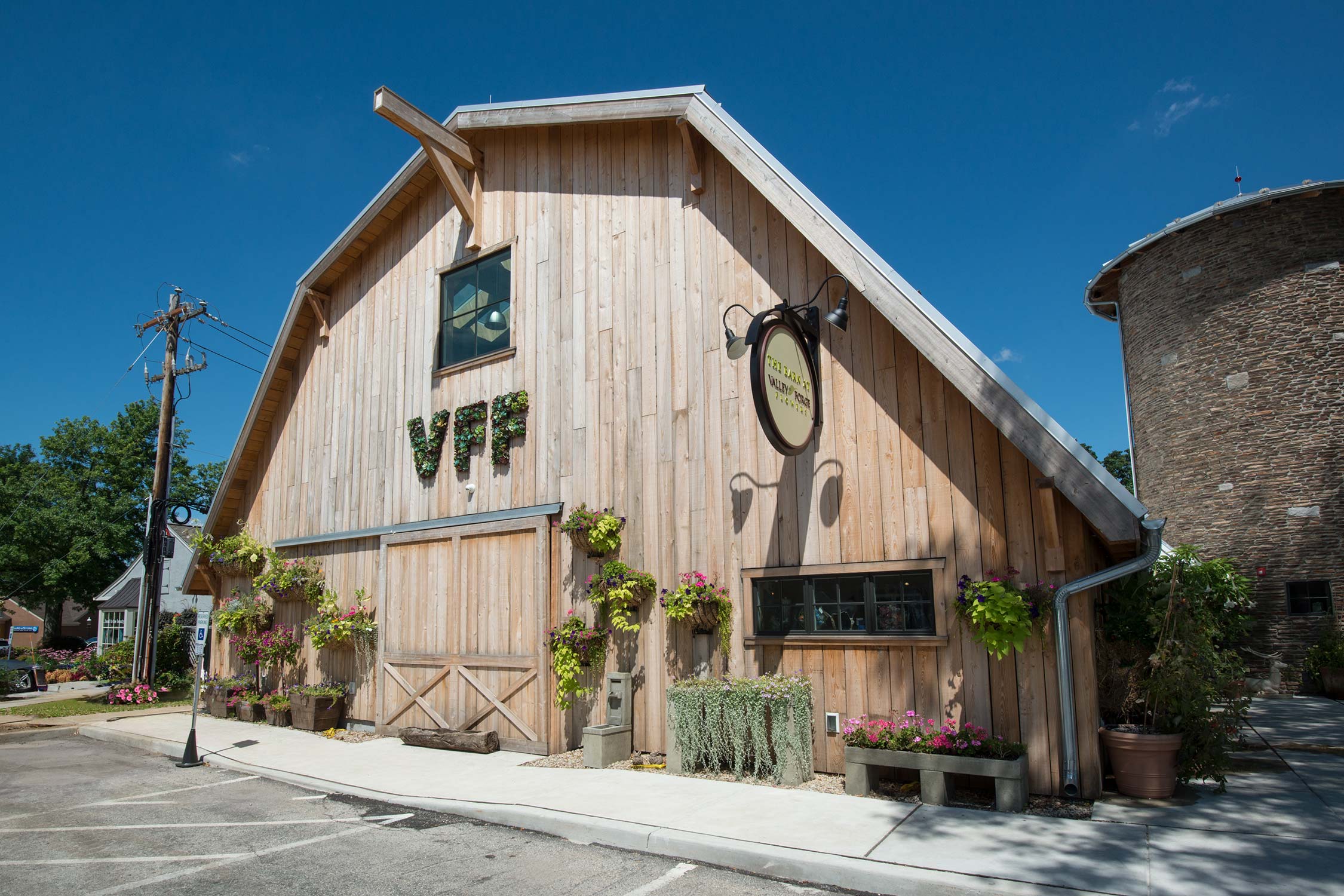 Valley Forge Flowers in Wayne, PA: a stone silo and barn-style building with a metal roof, surrounded by potted plants and trees on a sunny day.