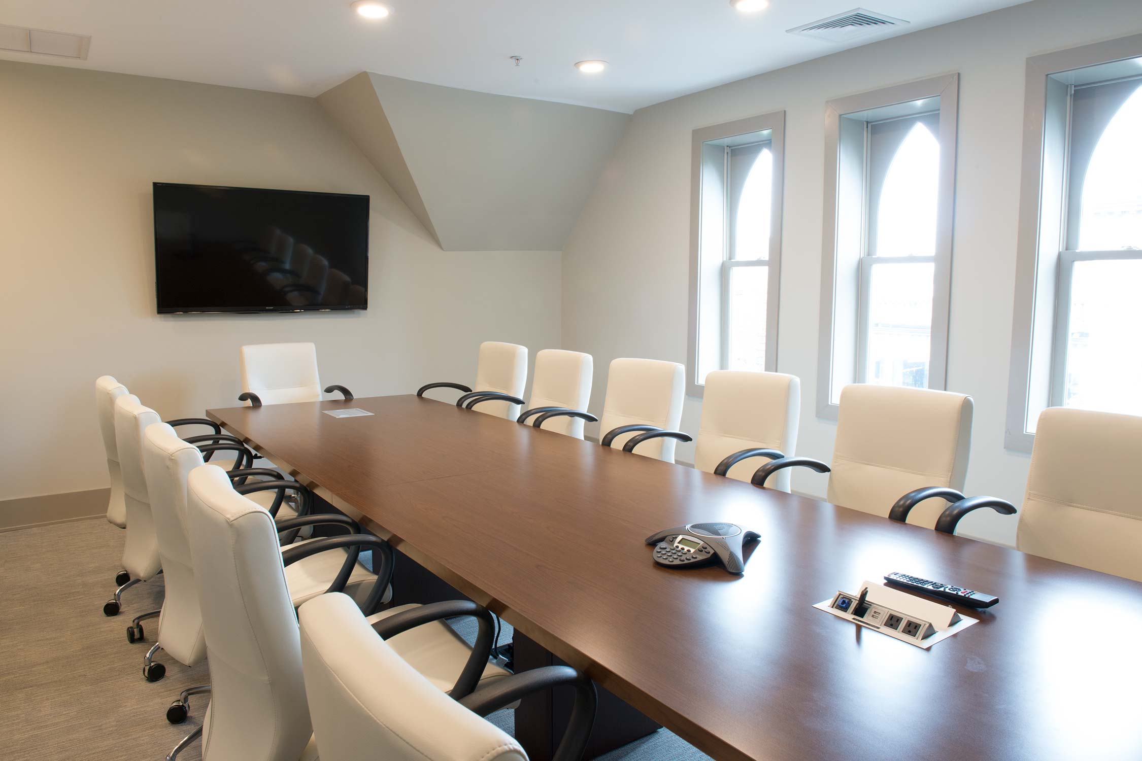 Conference room with wooden table, white chairs, TV, and large arched windows.