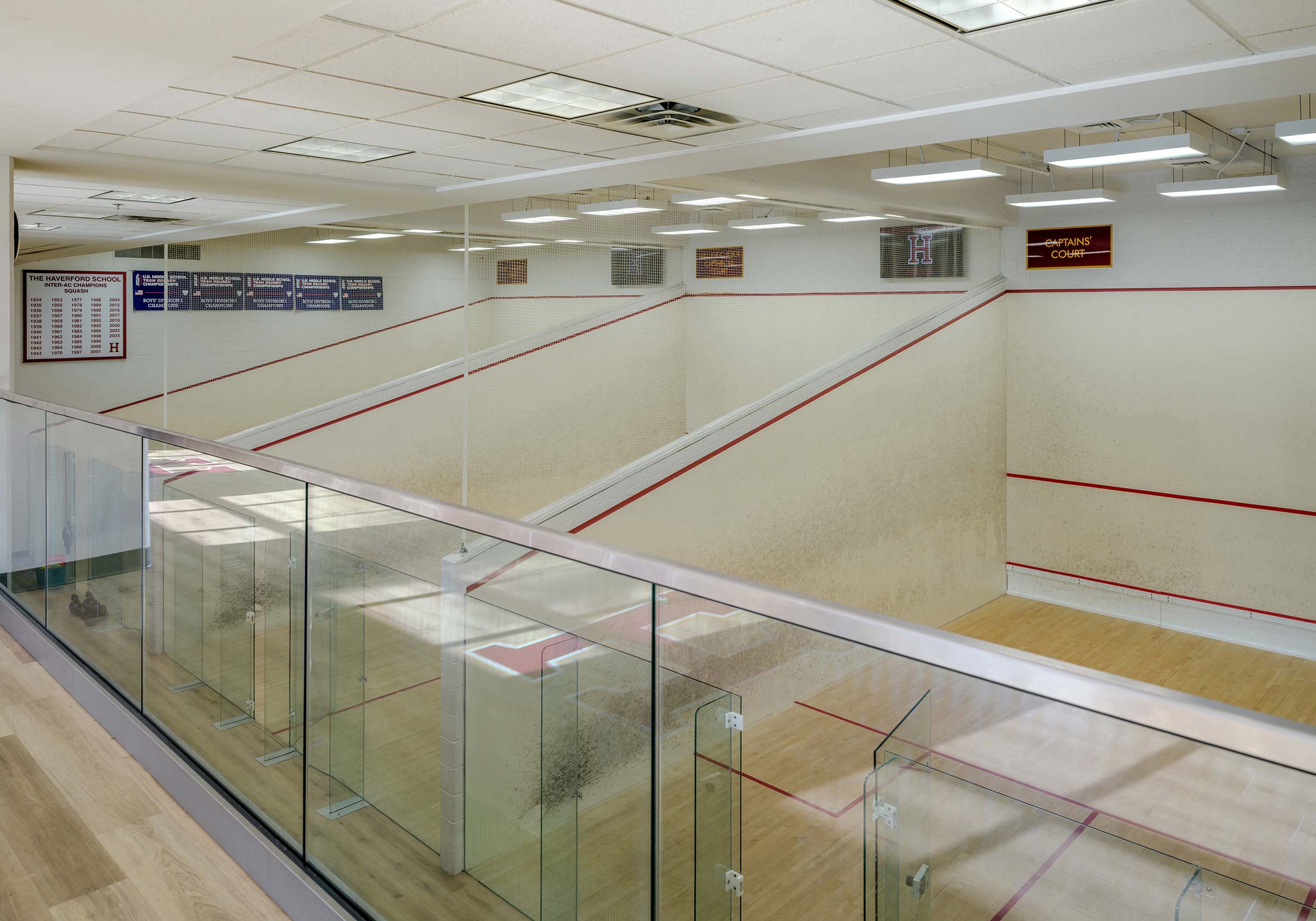 Squash courts at The Haverford School with glass walls and viewing area. Walls display championship banners and a