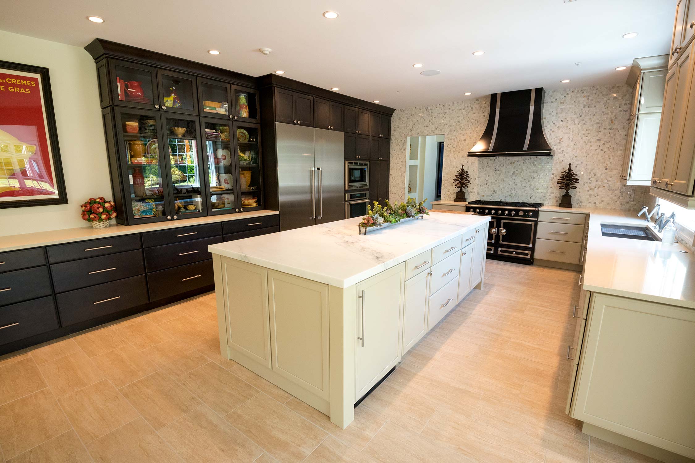 Spacious kitchen featuring marble island, dark glass-front cabinets with vibrant dishware, stainless steel appliances, and black range hood.