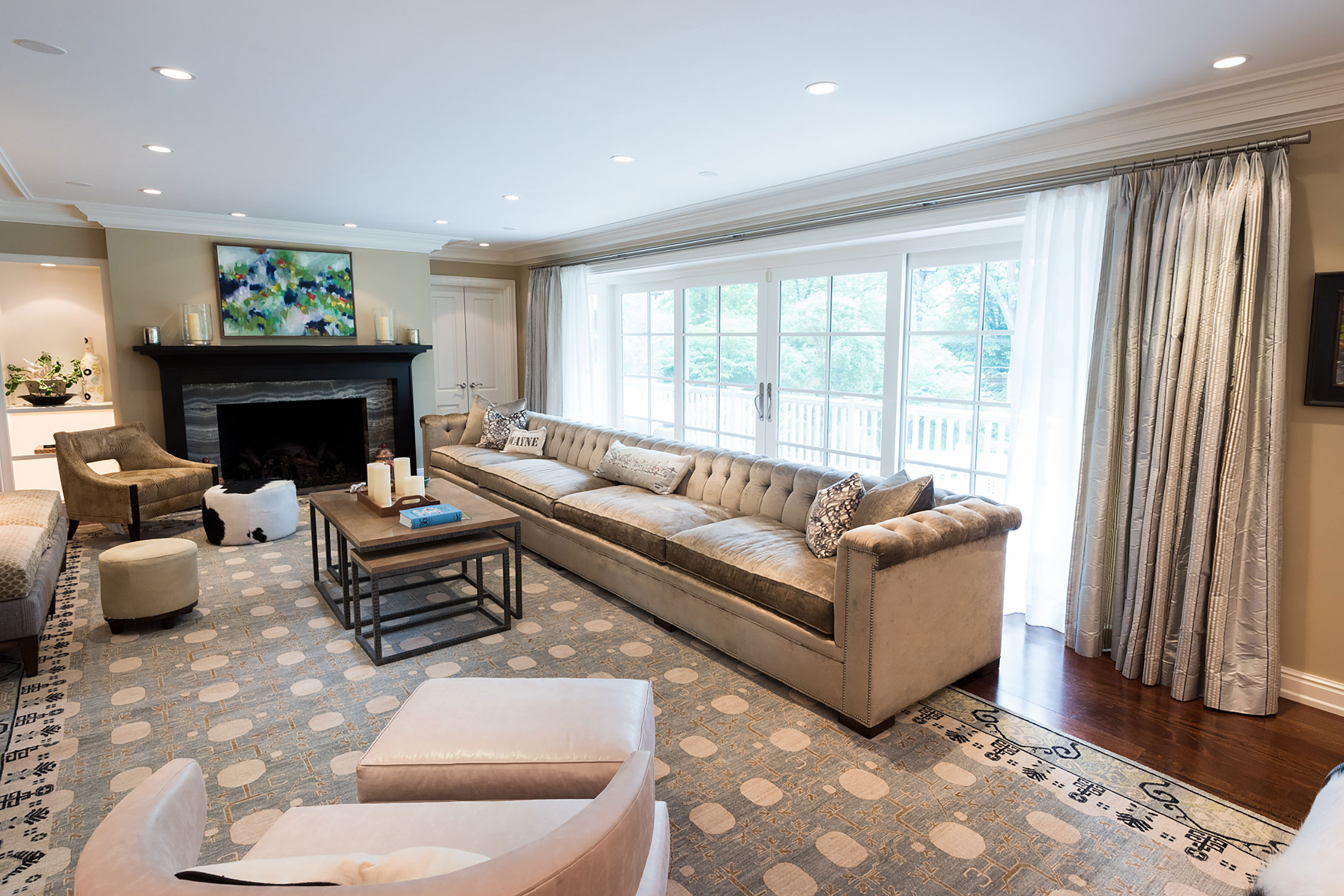 Elegant living room with a spacious tufted sofa, modern fireplace, and vibrant abstract art. Large windows provide lush views, enhanced by a patterned rug and cozy accents.