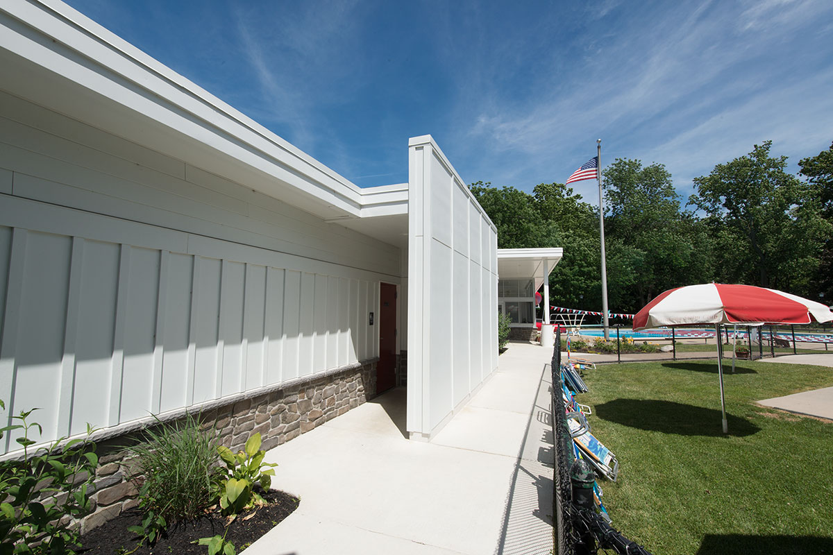 Swim club with white clubhouse, red umbrellas, flagpole, and pool area.
