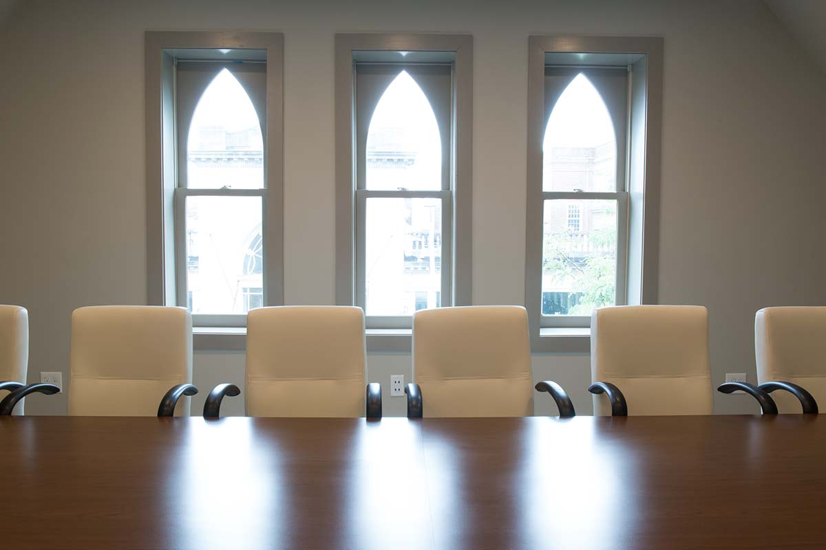 Conference room with wooden table, white chairs, and large arched windows.
