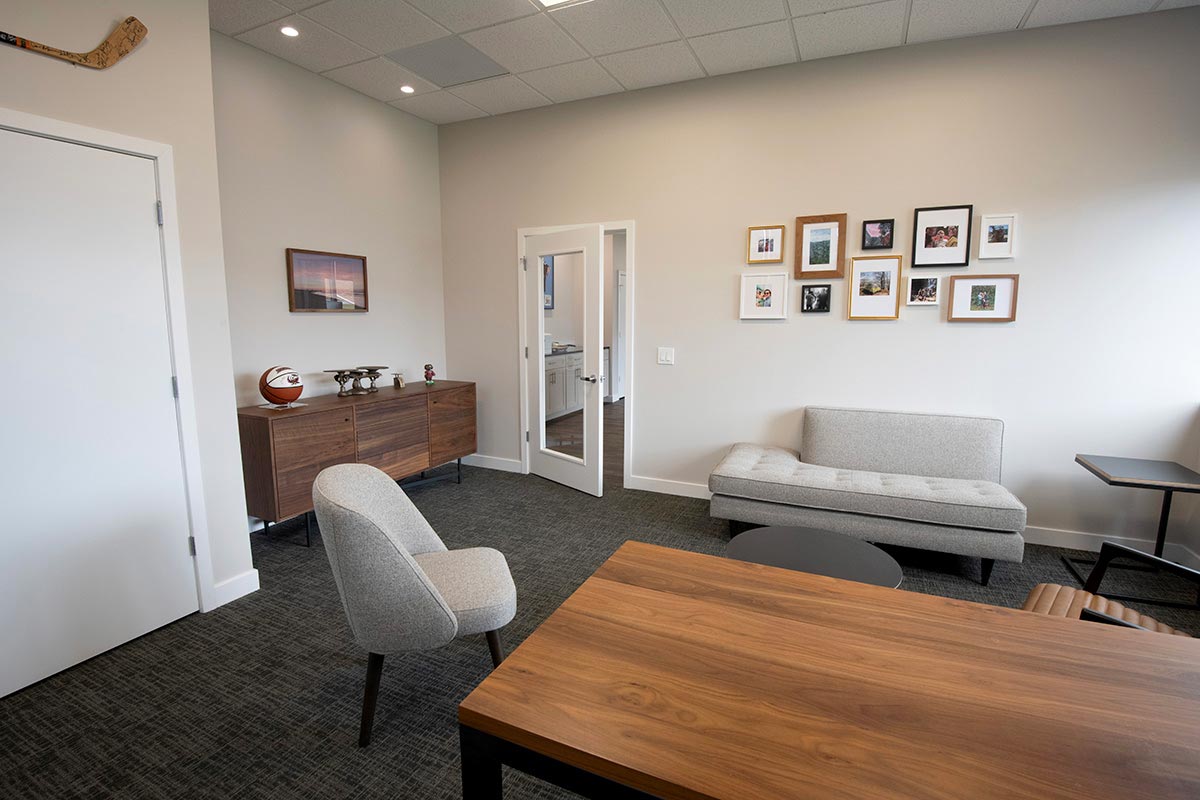 Modern office with wooden desk, gray chair, sofa, framed photos on wall, and hockey stick decor.