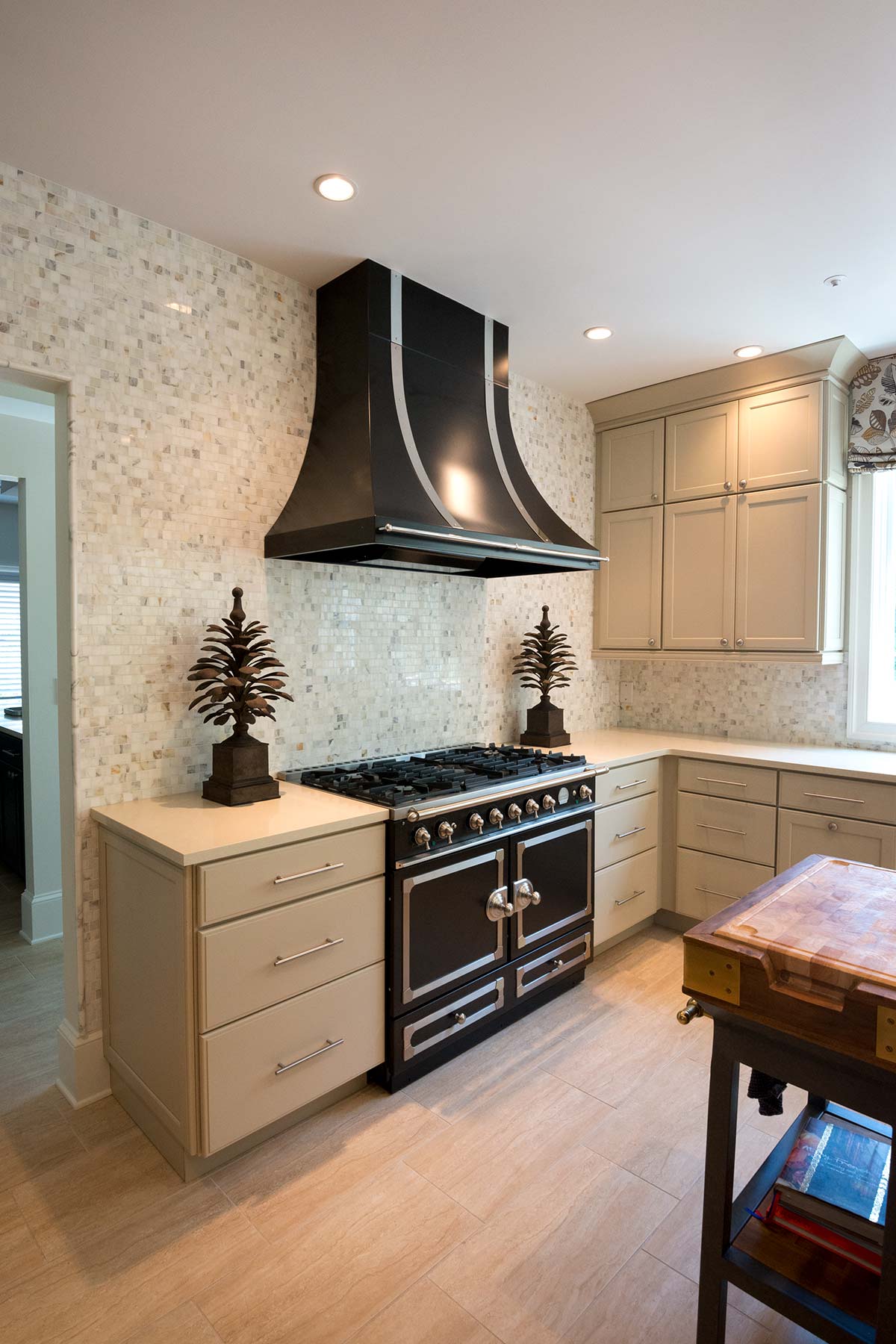 Modern kitchen with a sleek black range and hood, light cabinets, mosaic tile backsplash, and a wooden cutting board station.