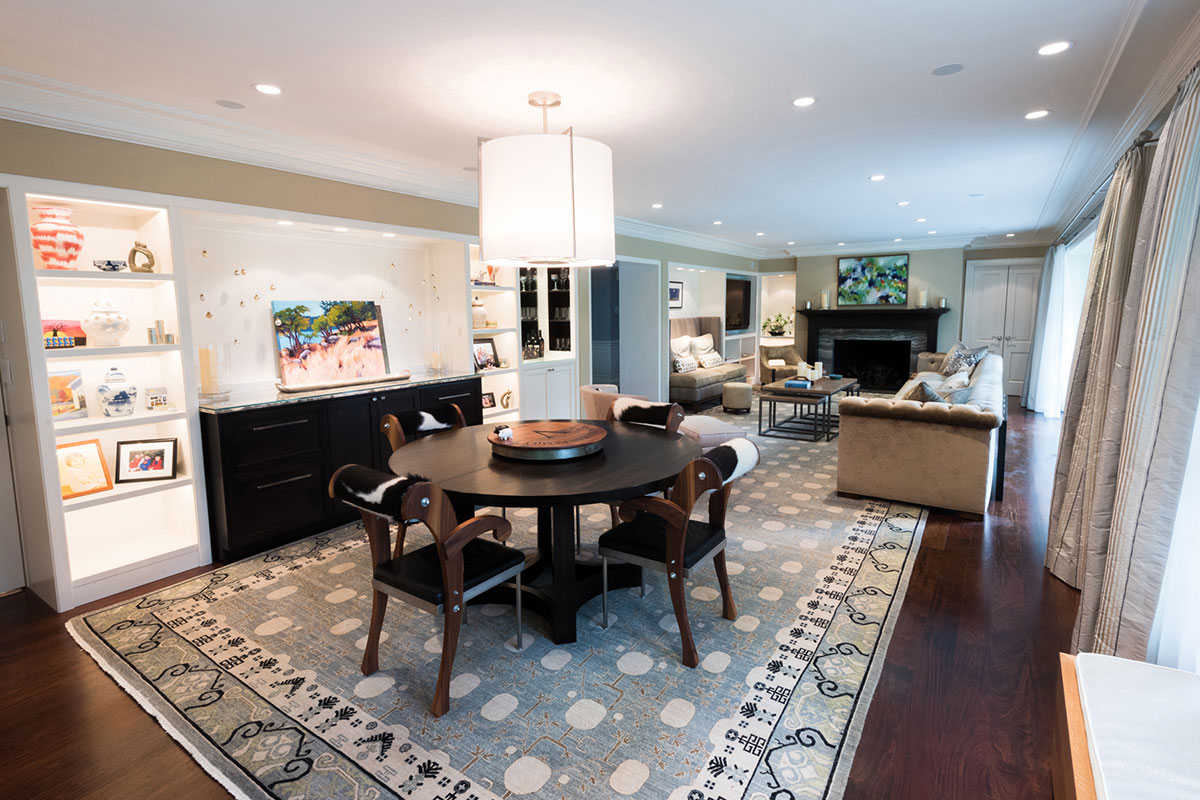 Elegant dining area with a modern round table, chic chairs, and a stylish rug. Features a cozy living space with a fireplace, artwork, and shelves with decor.