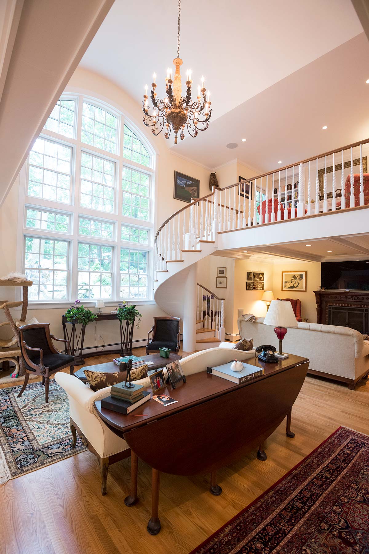 pacious living room with high ceilings, a grand chandelier, and a spiral staircase. Features elegant furniture, large windows, and a cozy fireplace. Ideal for gatherings.