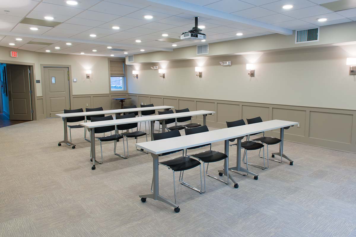 Meeting room with white tables, black chairs, projector, and wall sconces.