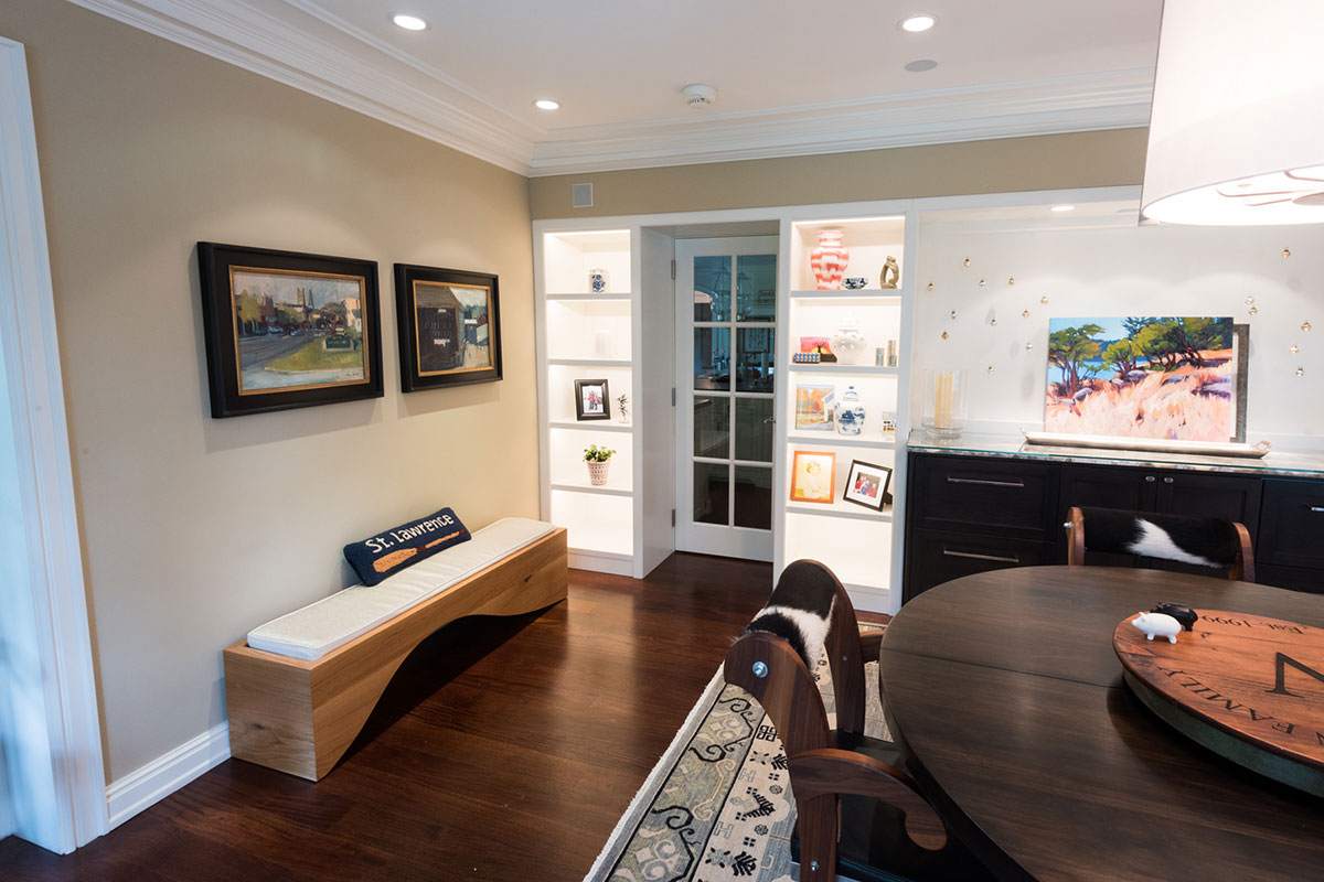 Stylish dining area with a round table, unique chairs, and a modern bench. Features art-filled shelves and a cozy rug, blending elegance and comfort.