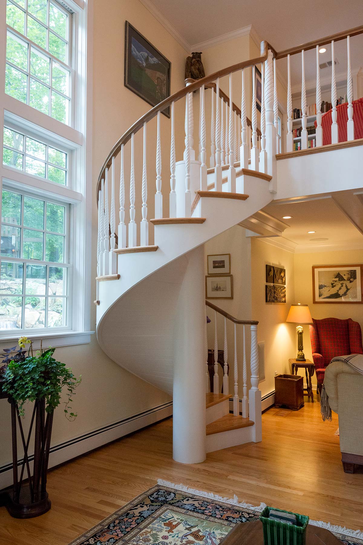 Stylish interior with a grand spiral staircase, large windows, and warm lighting. Features elegant decor, plants, and a cozy seating area. Perfect for a chic home.