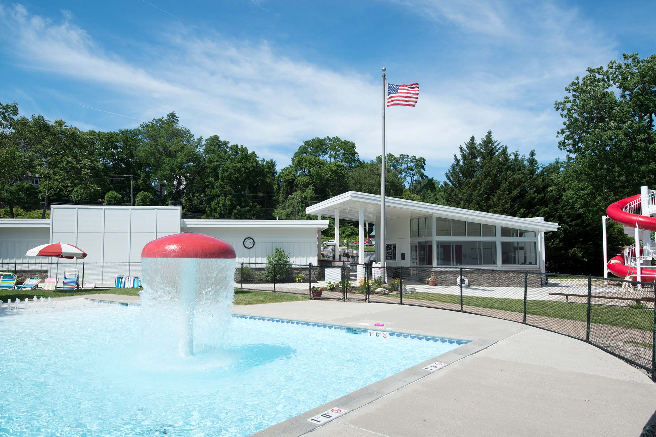 Kiddie pool with water fountain umbrellas, lounge chairs, and white clubhouse.