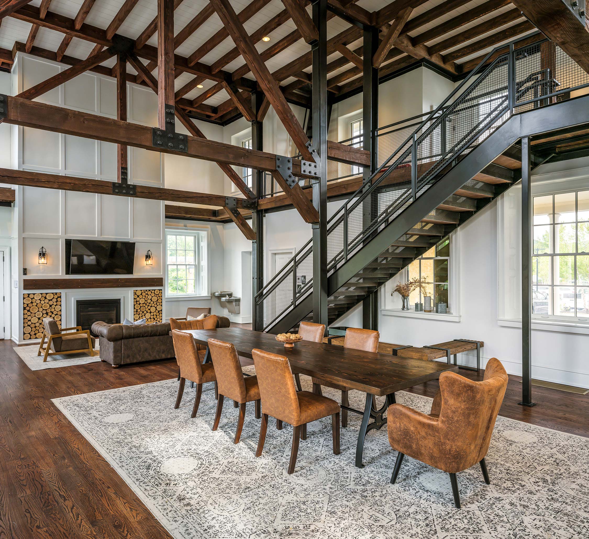 Spacious room with wooden beams, metal staircase, dining table, leather chairs, sofa, fireplace, and TV.
