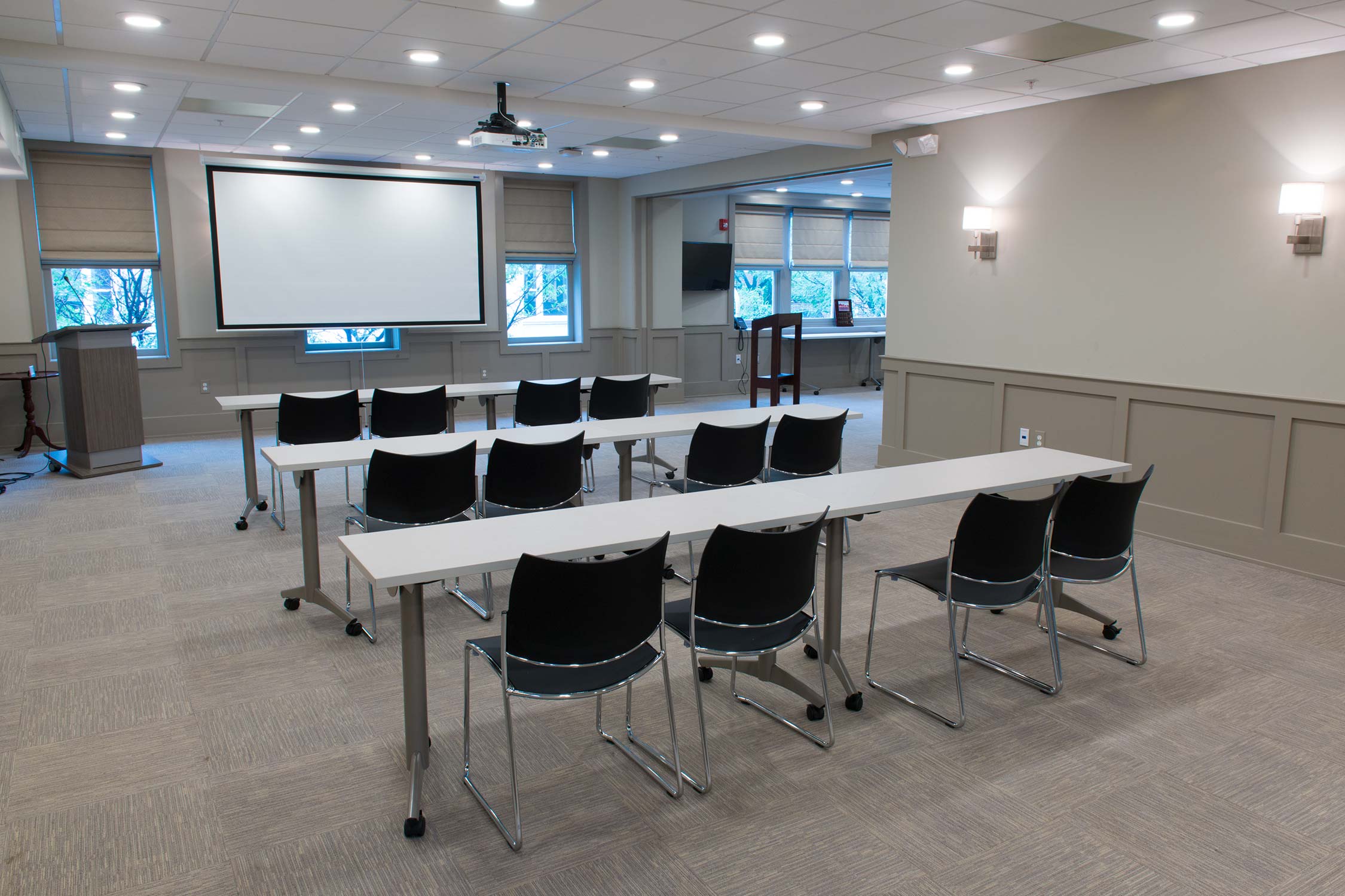 Meeting room with white tables, black chairs, projector screen, and wall sconces.
