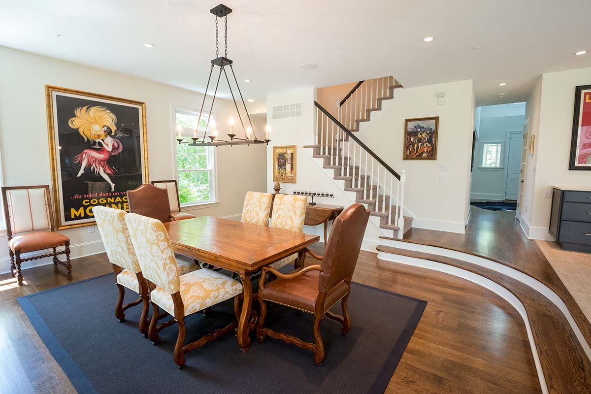 Elegant dining room with wooden table, upholstered chairs, vintage chandelier, and vibrant wall art near a staircase.