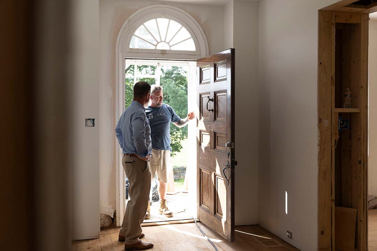 Andy Kerns and a Ranieri & Kerns superintendent talking at an open wooden door with a semi-circle window in a home under construction.