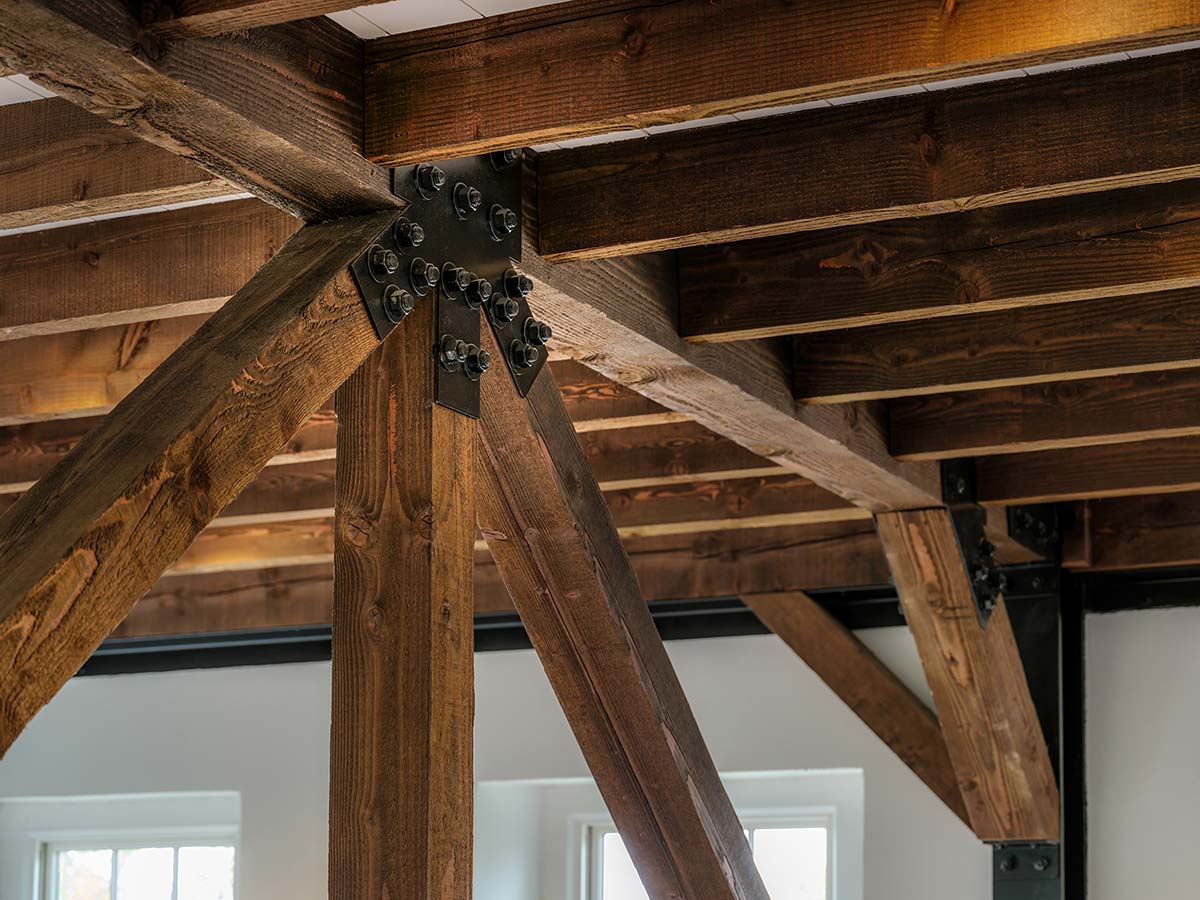Wooden ceiling beams with metal brackets in a room with white walls and large windows.