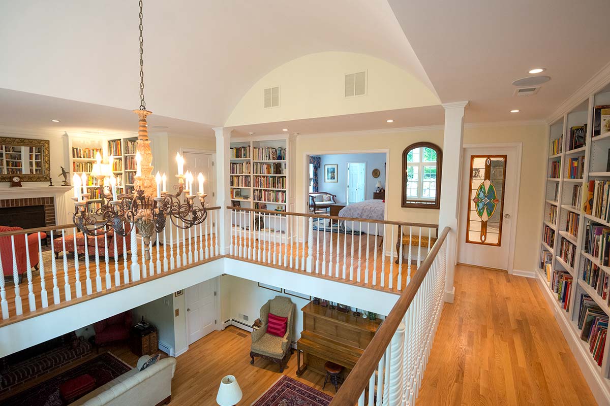 Elegant two-story library with chandelier, bookshelves, and cozy furniture. Features hardwood floors, arched ceiling, and a stained-glass door.