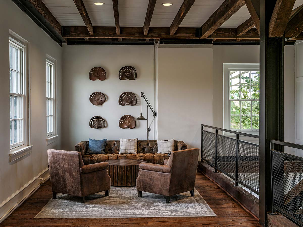 Cozy room with wooden beams, leather sofa, chairs, coffee table, and vintage farm decor on the wall.