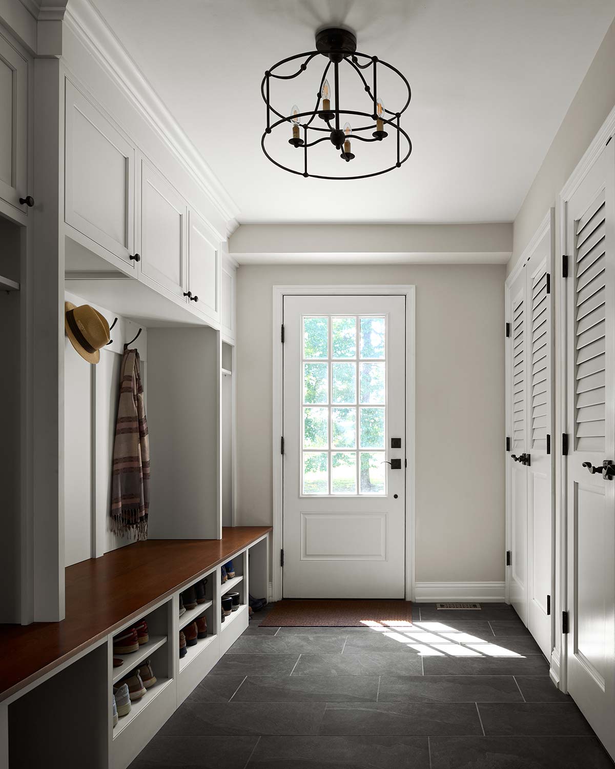 Mudroom with white cabinets, wooden bench, shoes, hat, scarf, and glass door with natural light.
