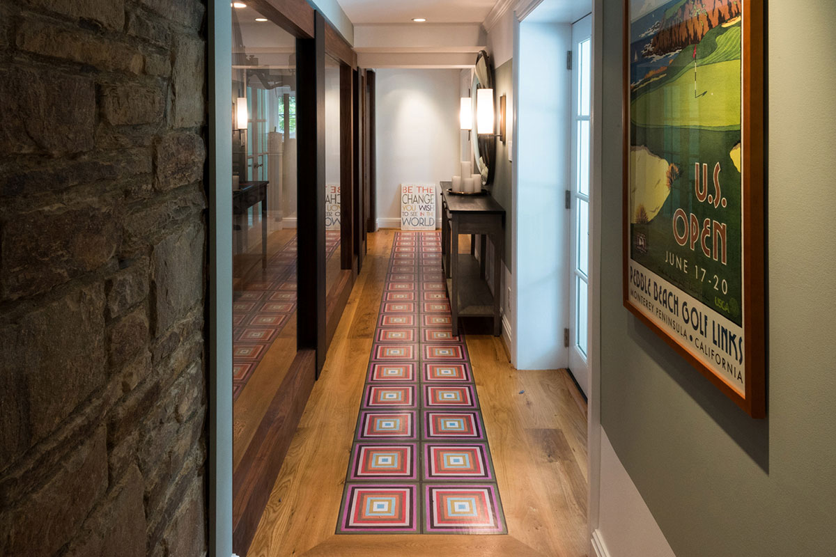Stylish hallway with a colorful geometric rug, mirrored walls, and a vintage U.S. Open poster. Features a sleek console table and soft lighting.