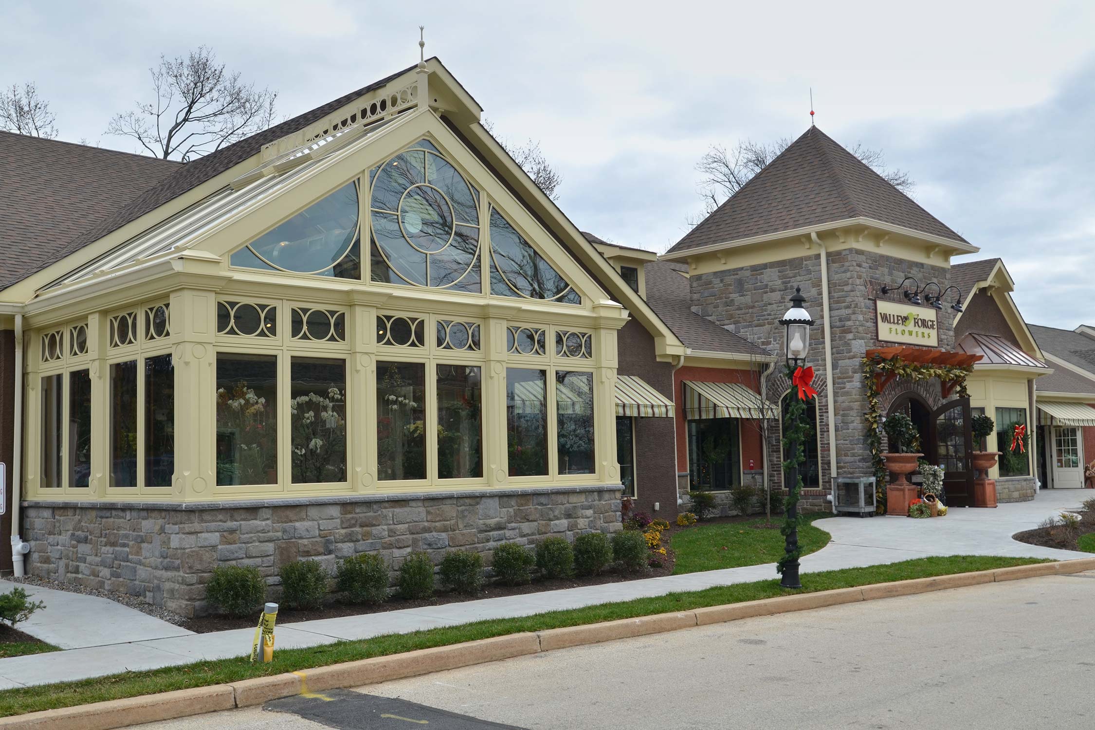 Valley Forge Flowers with a stone facade, glass conservatory, striped awnings, and holiday decor under an overcast sky.