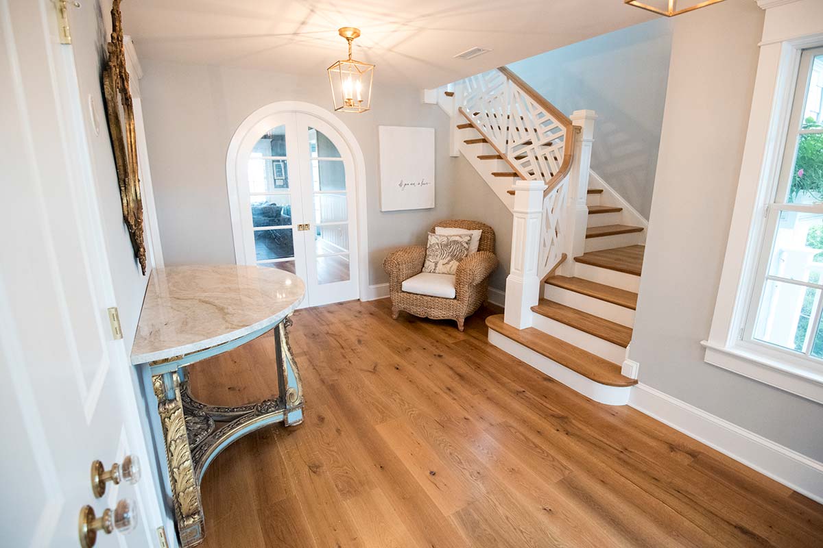 A cozy entryway with a wooden staircase, wicker chair, marble console table, ornate mirror, and a lantern light.