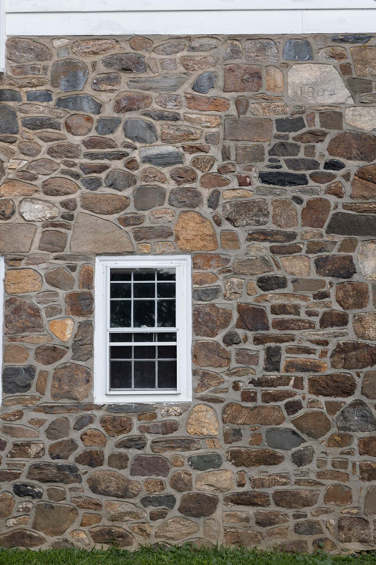 Stone wall with a white-framed window, dated