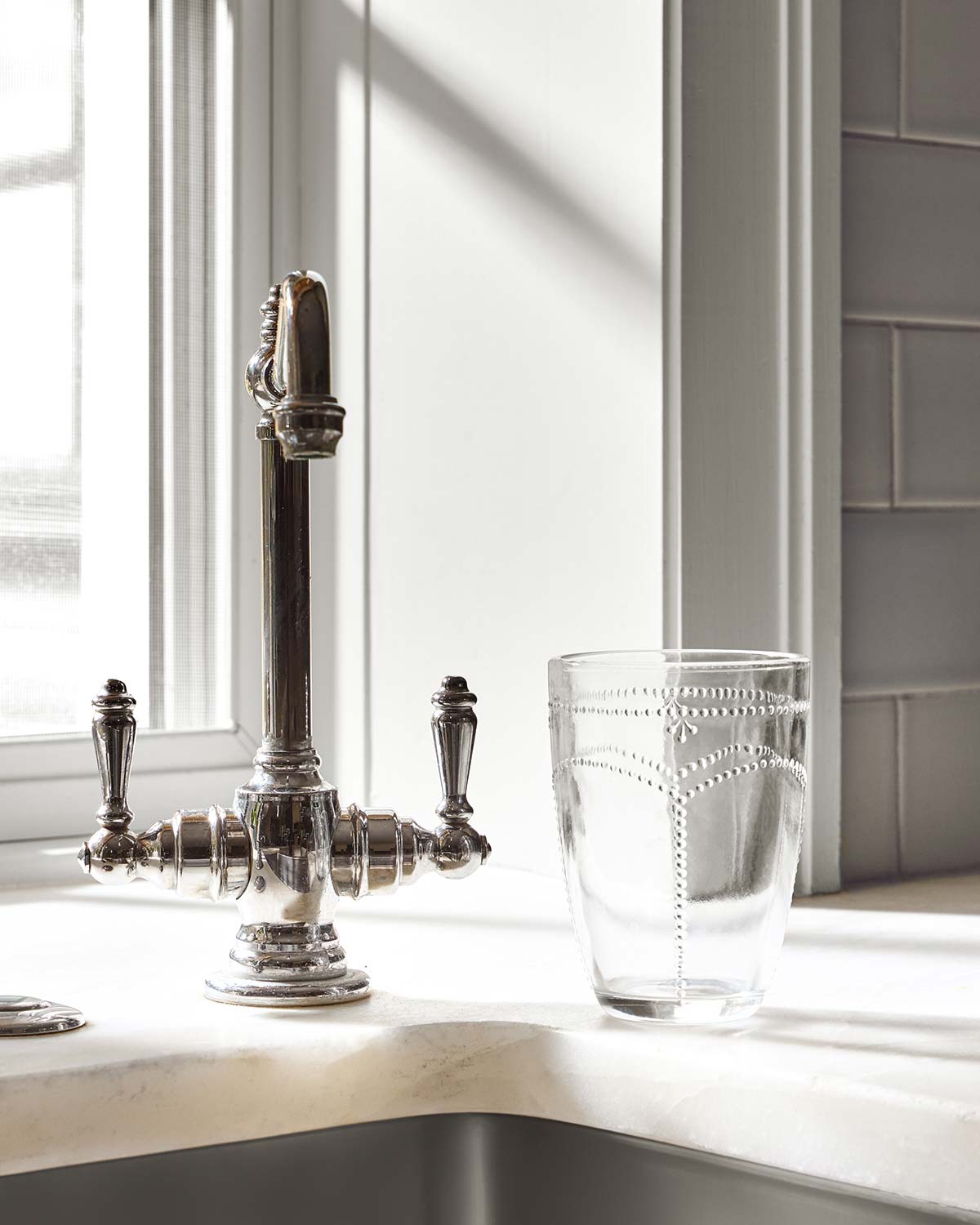 Kitchen counter with a polished silver faucet, a clear glass with etched design, and white subway tile backsplash.