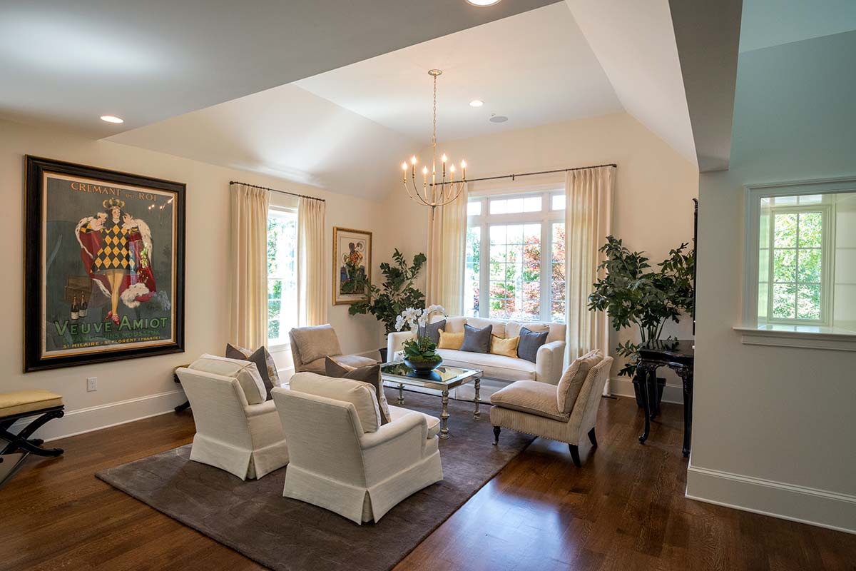 Bright living room with elegant seating, chandelier, large windows, vibrant wall art, and lush plants on wooden flooring.