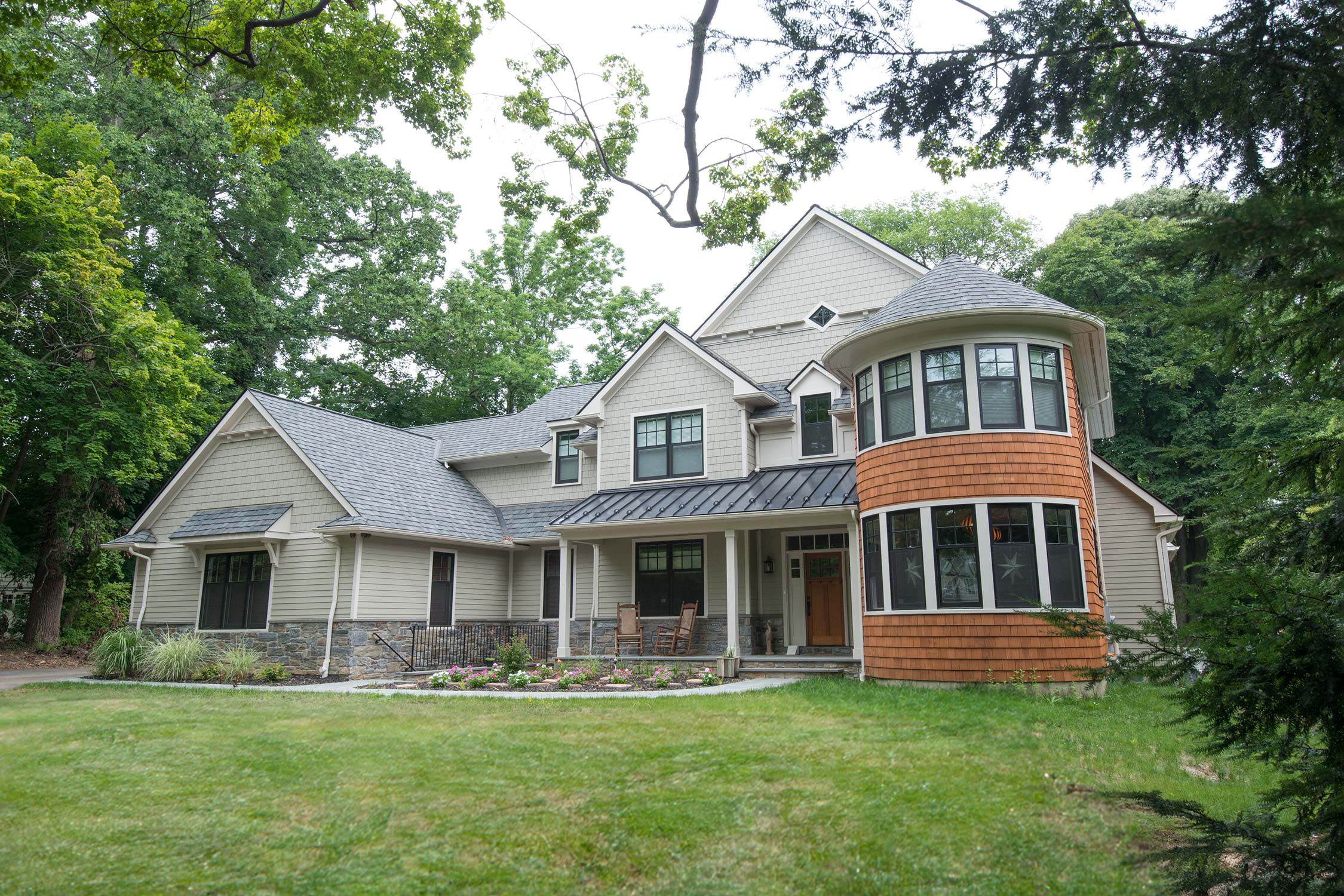 Spacious modern home with a curved orange facade, surrounded by lush greenery and a welcoming front porch.