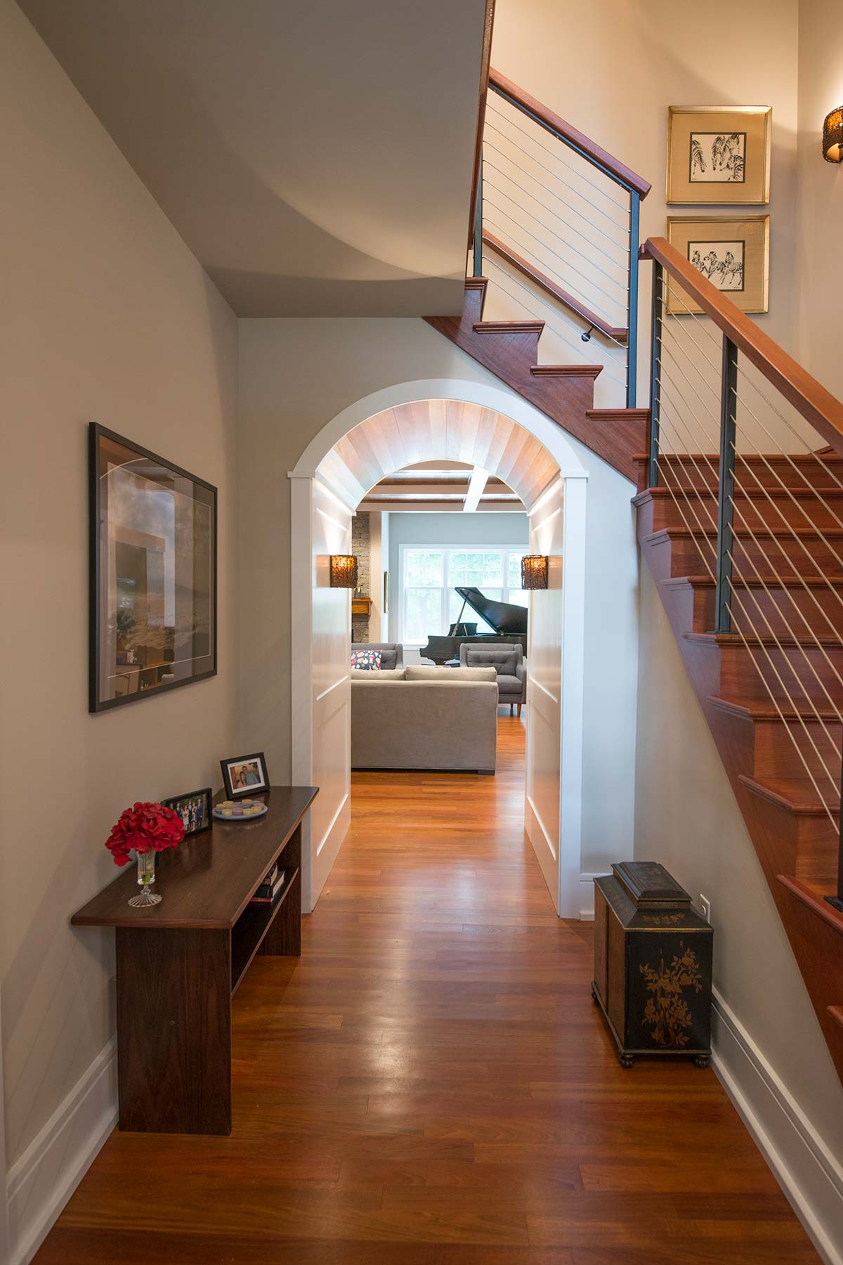 Elegant hallway with wooden staircase, arched ceiling, and a view into a cozy living room with a piano.