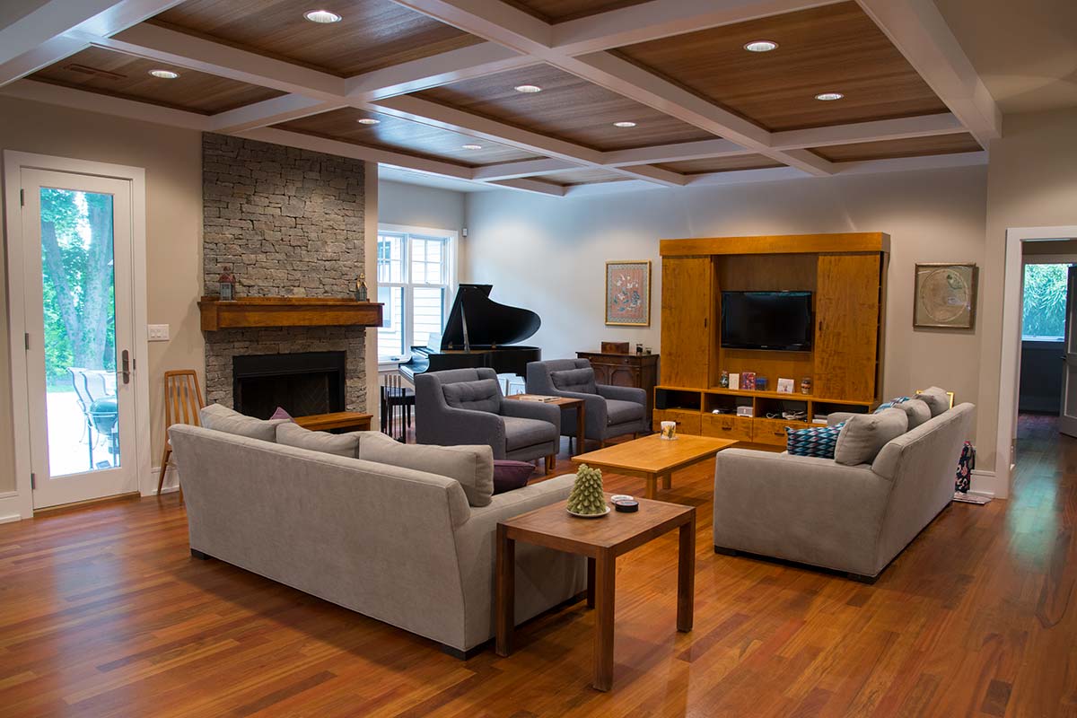 Spacious living room with wooden ceiling, stone fireplace, grand piano, and cozy gray sofas.