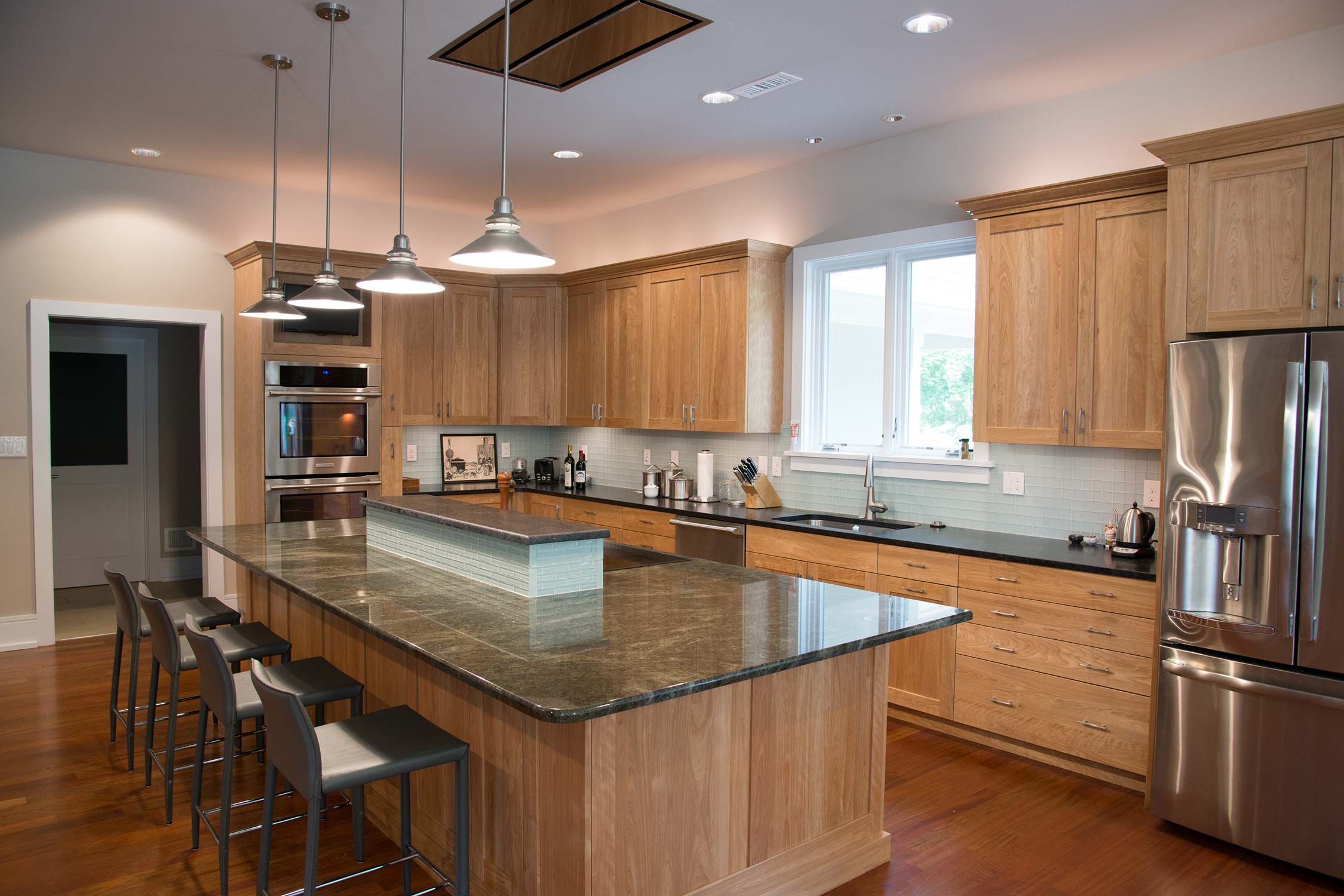 Modern kitchen with wooden cabinets, granite island, and stainless steel appliances, featuring pendant lighting.