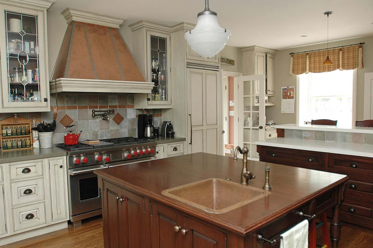 Cozy kitchen with dark wood island, copper sink, and white cabinets. Features a copper hood, red stove, and large windows for natural light.