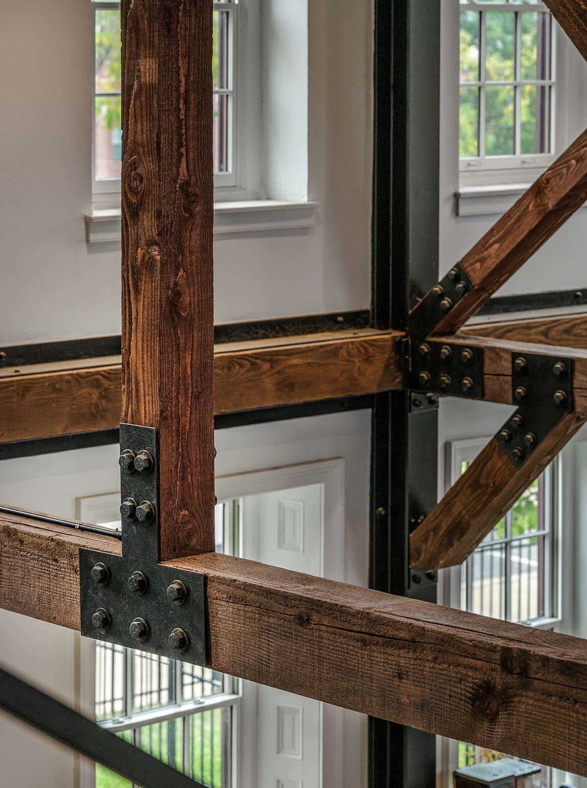 Wooden beams with metal brackets in a room with white walls, large windows, and a white door.