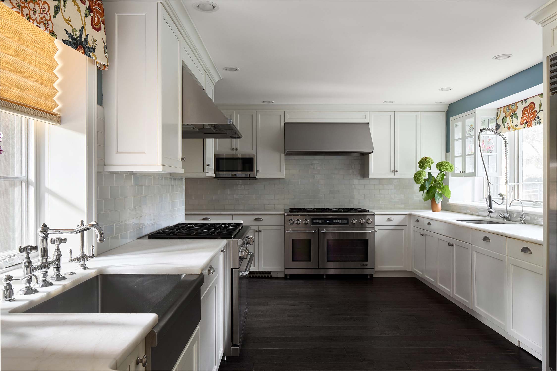 Modern kitchen with white cabinets, stainless steel appliances, marble counters, subway tile backsplash, and floral window shades.
