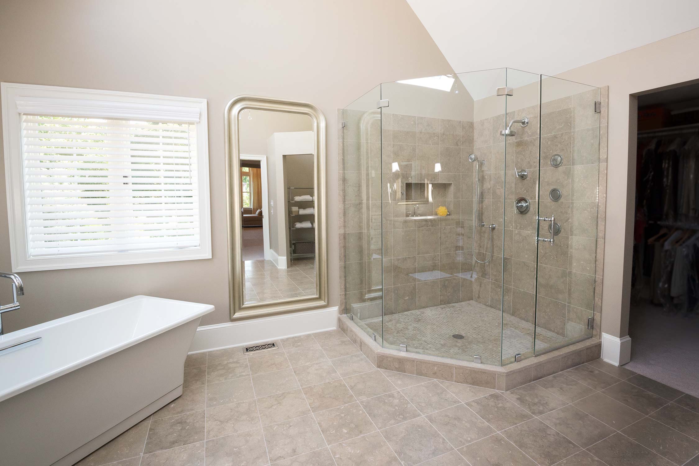 Luxurious bathroom with freestanding tub, glass-enclosed shower with multiple heads, large mirror, and natural light from a window.