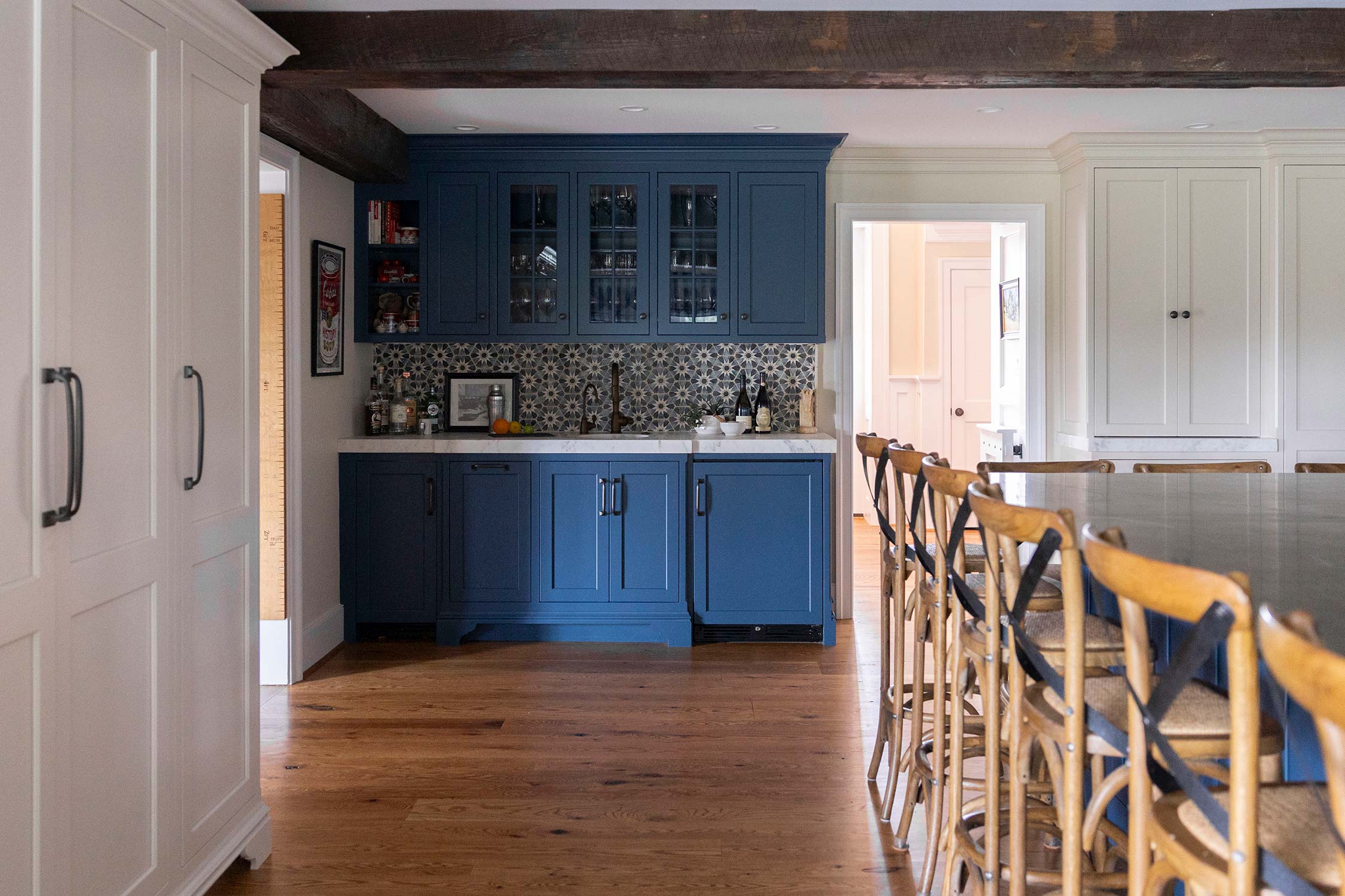 Stylish kitchen with blue cabinets, glass doors, and patterned tile backsplash. Wooden chairs line an island, with white cabinets and wood floor.