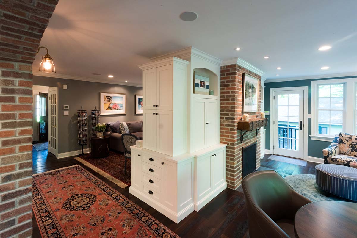 Cozy living room with white cabinetry, brick fireplace, and vibrant rug, featuring modern furniture and large windows with natural light.
