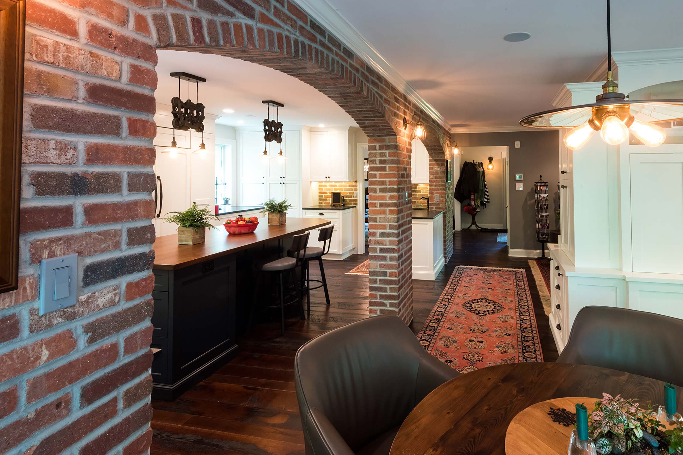 Stylish open-plan kitchen with brick arches, wooden island, modern lighting, and cozy dining area with a vibrant rug.