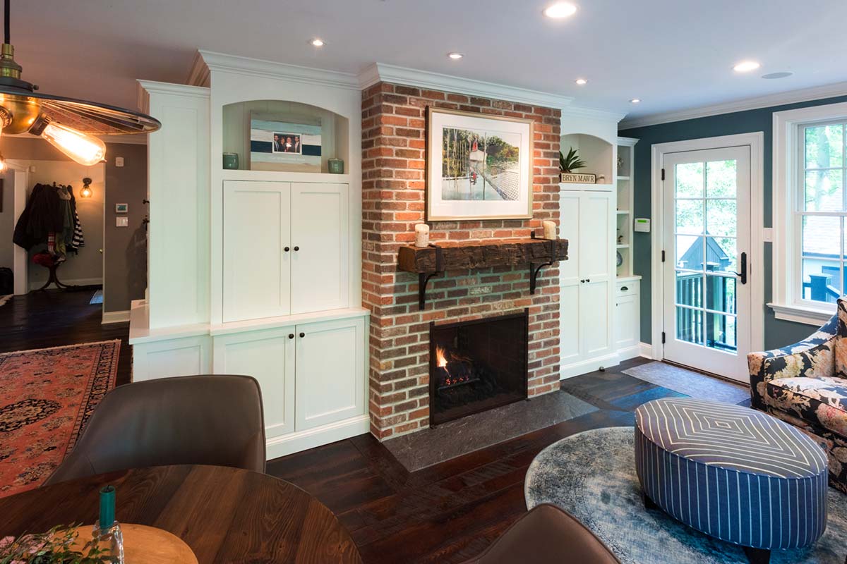 Warm living room with brick fireplace, white cabinetry, and modern decor, featuring a cozy fire and large windows with natural light.