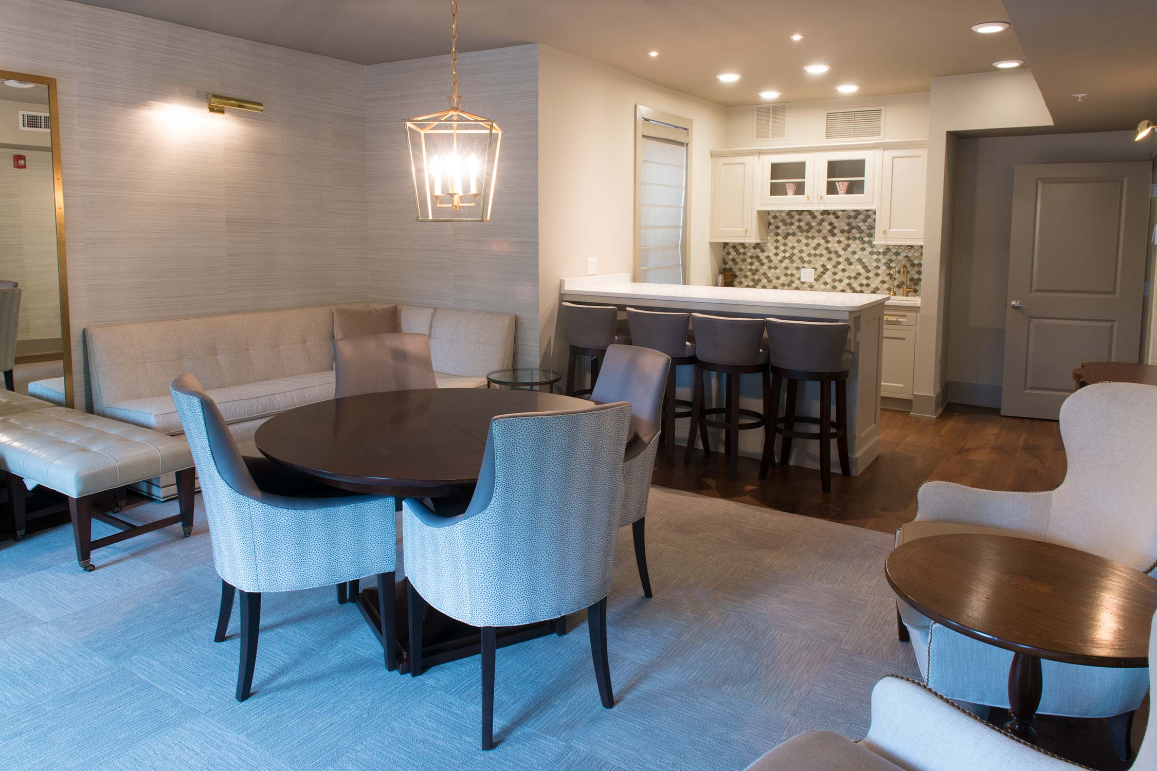Modern lounge with round table, chairs, sofa, bar counter, and chandelier.